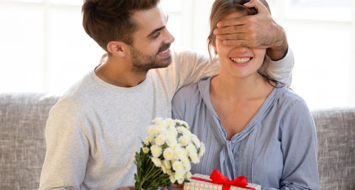 Женщина закрывает мужчине глаза и дарит подарок